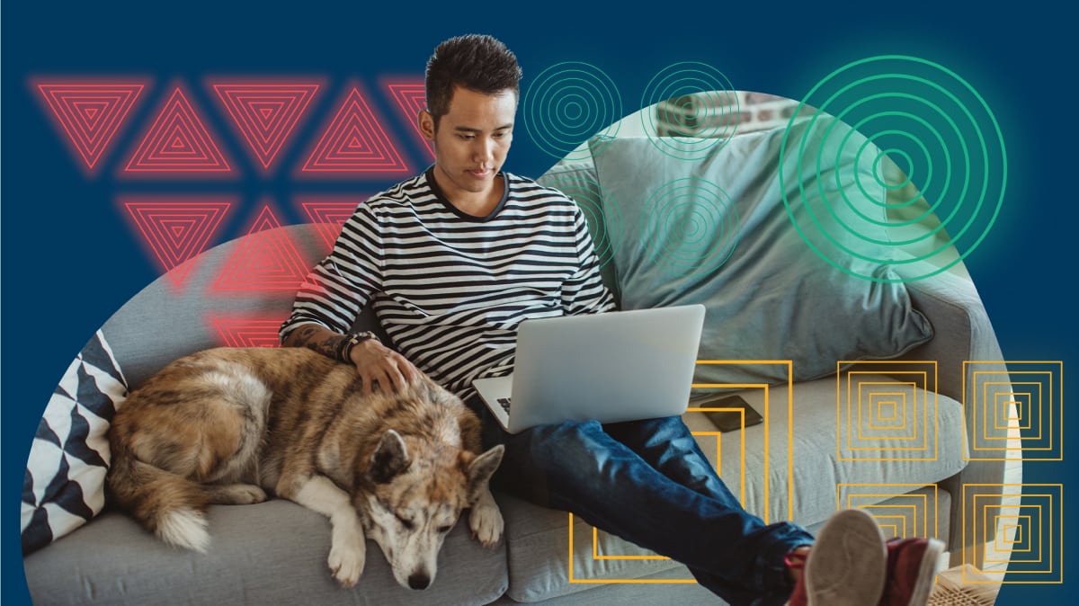 A man on the couch with his dog looking at his laptop.